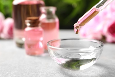 Photo of Dripping rose essential oil into bowl on table, space for text