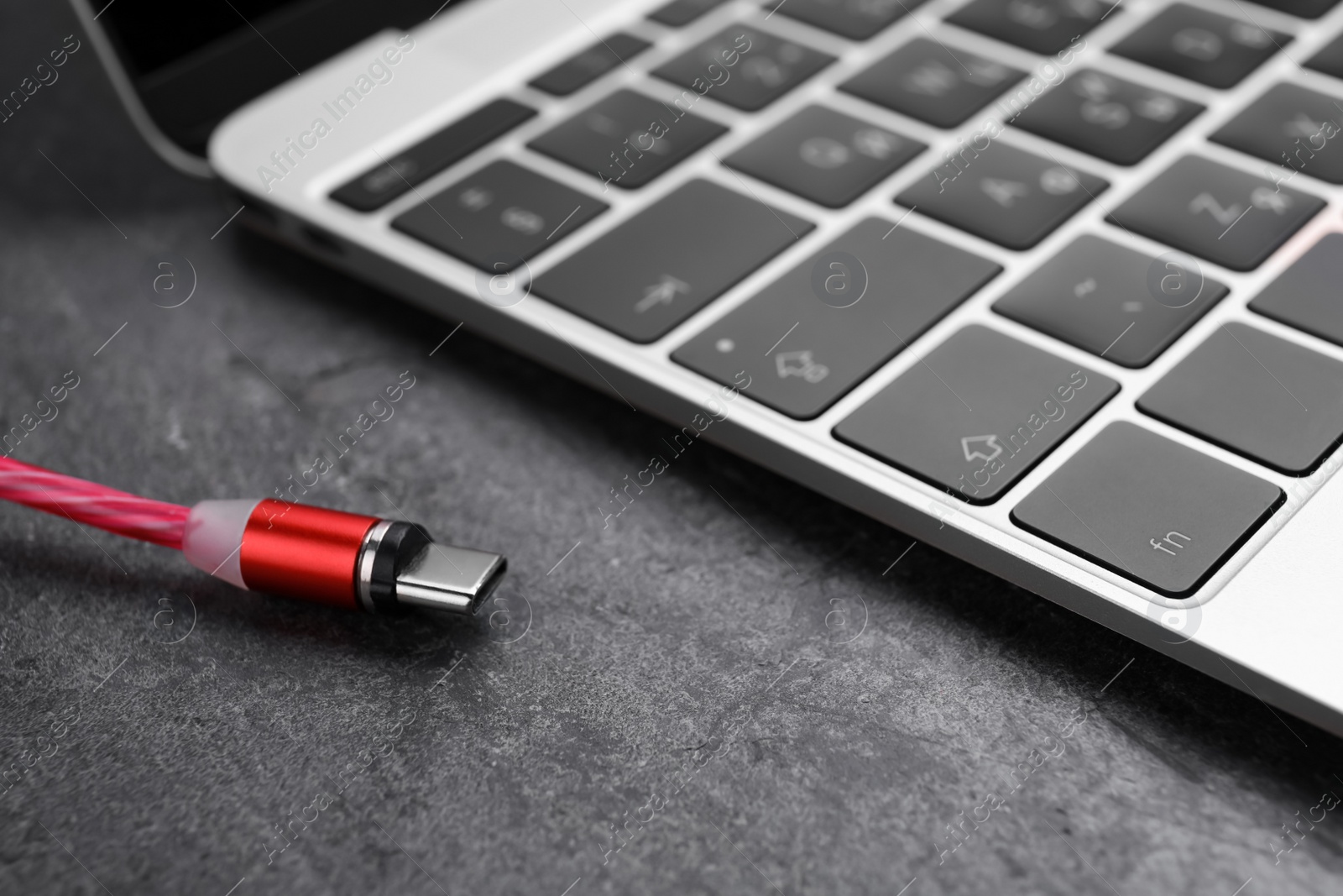 Photo of USB cable with type C connector and laptop on grey table, closeup