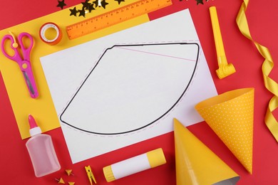 Photo of Handmade party hat template and supplies on red background, flat lay