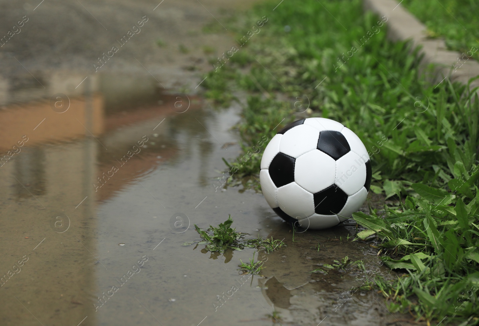 Photo of Soccer ball in puddle outdoors, space for text