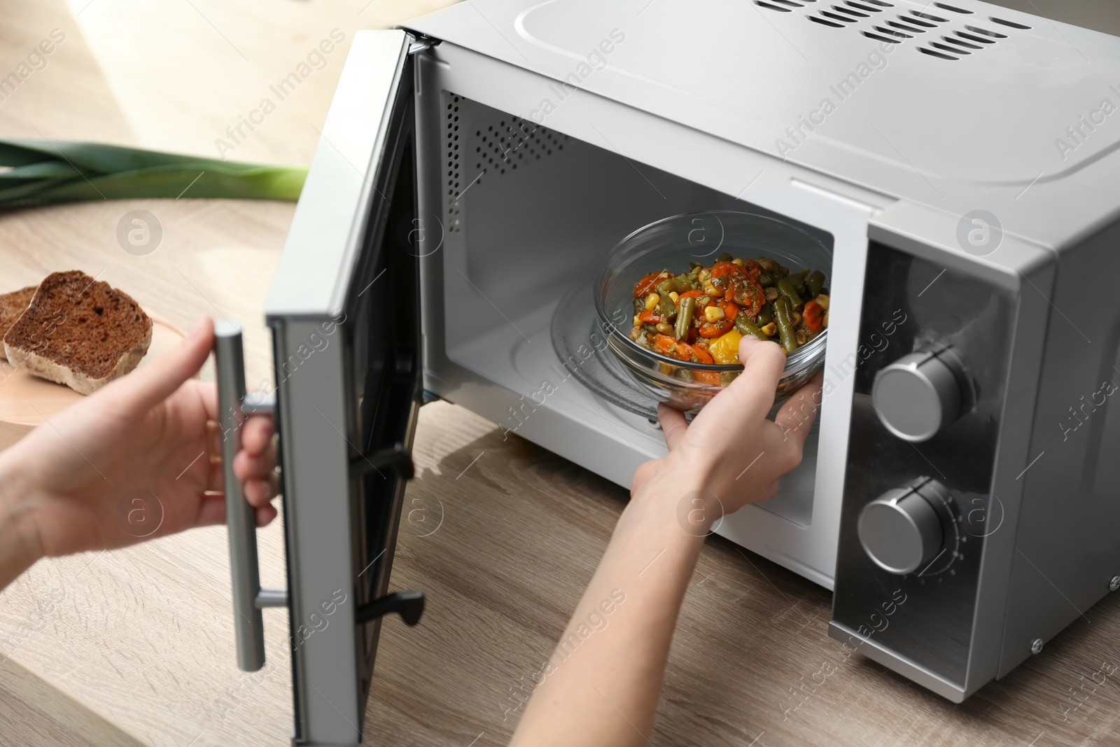 Photo of Young woman using microwave oven on table in kitchen