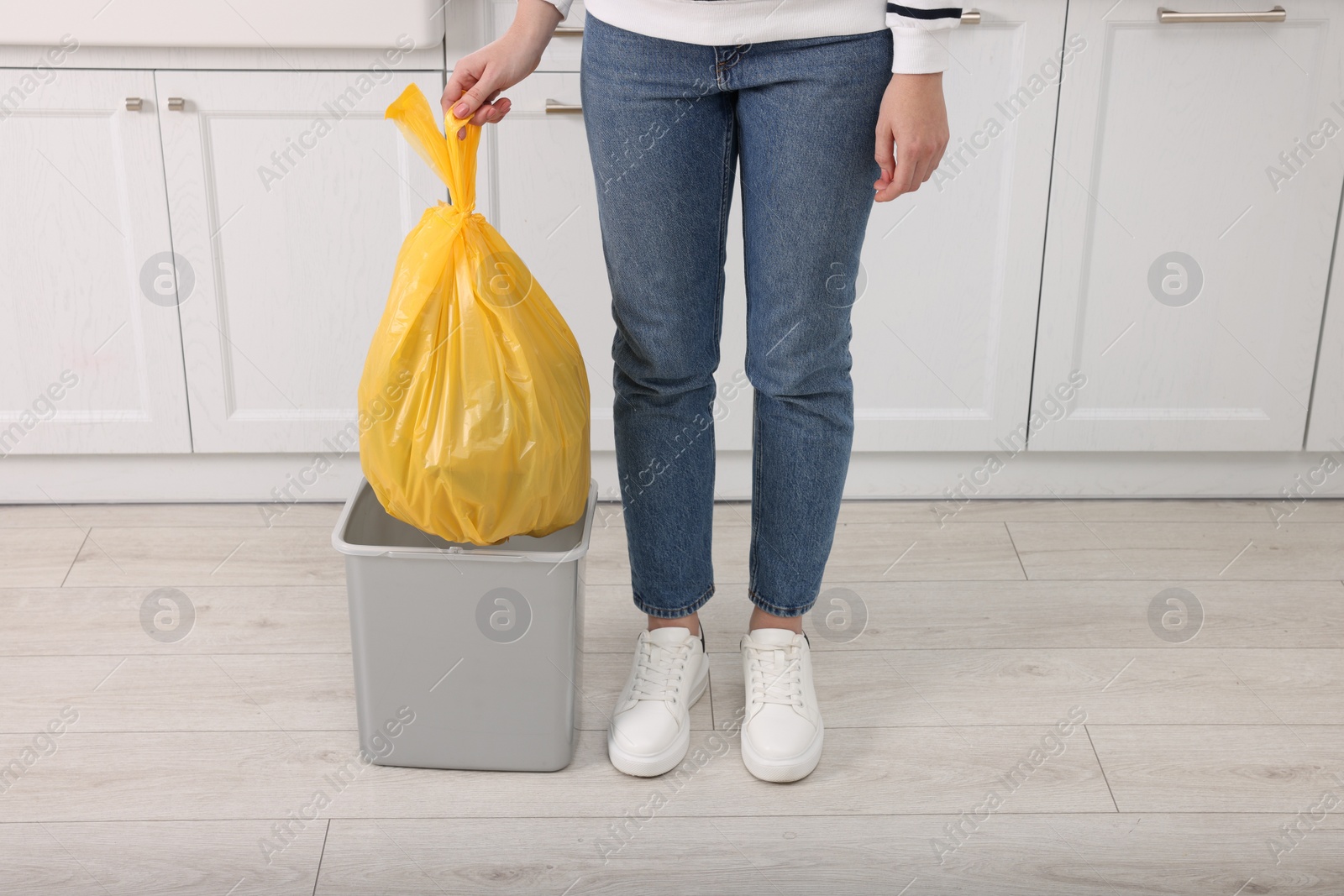 Photo of Woman taking garbage bag out of trash bin in kitchen, closeup