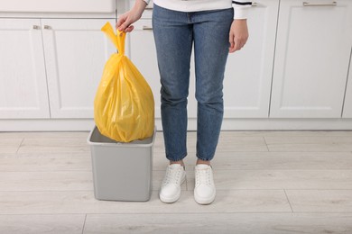 Photo of Woman taking garbage bag out of trash bin in kitchen, closeup