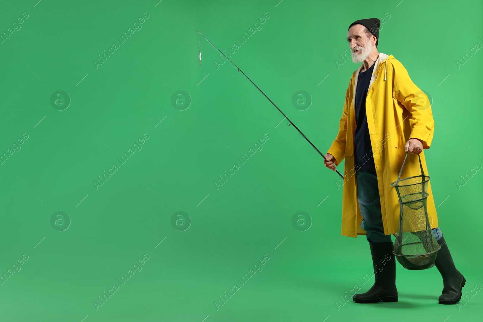 Photo of Fisherman holding rod and fishing net with catch on green background, space for text