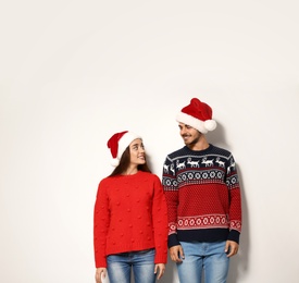 Young couple in warm sweaters and Christmas hats on white background