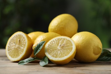 Fresh lemons and green leaves on wooden table, closeup