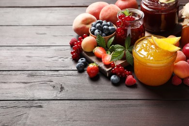Photo of Jars with different jams and fresh fruits on wooden table. Space for text