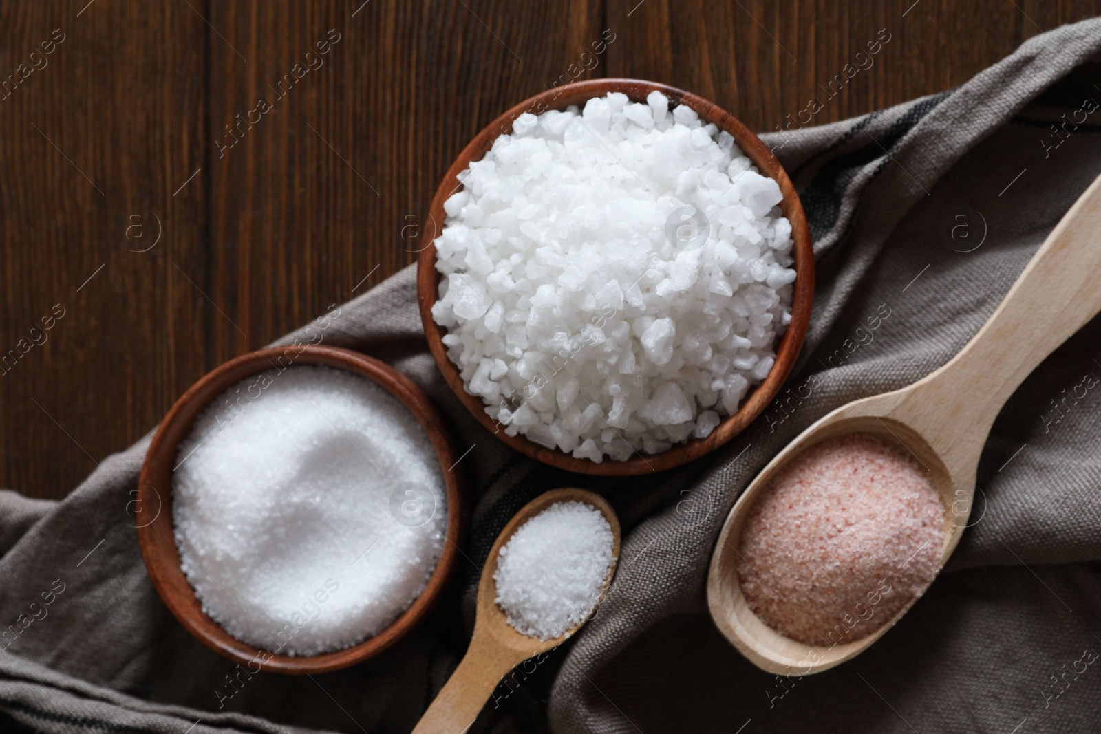 Photo of Different types of organic salt on wooden table, flat lay