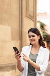 Photo of Beautiful young woman using smartphone near building outdoors