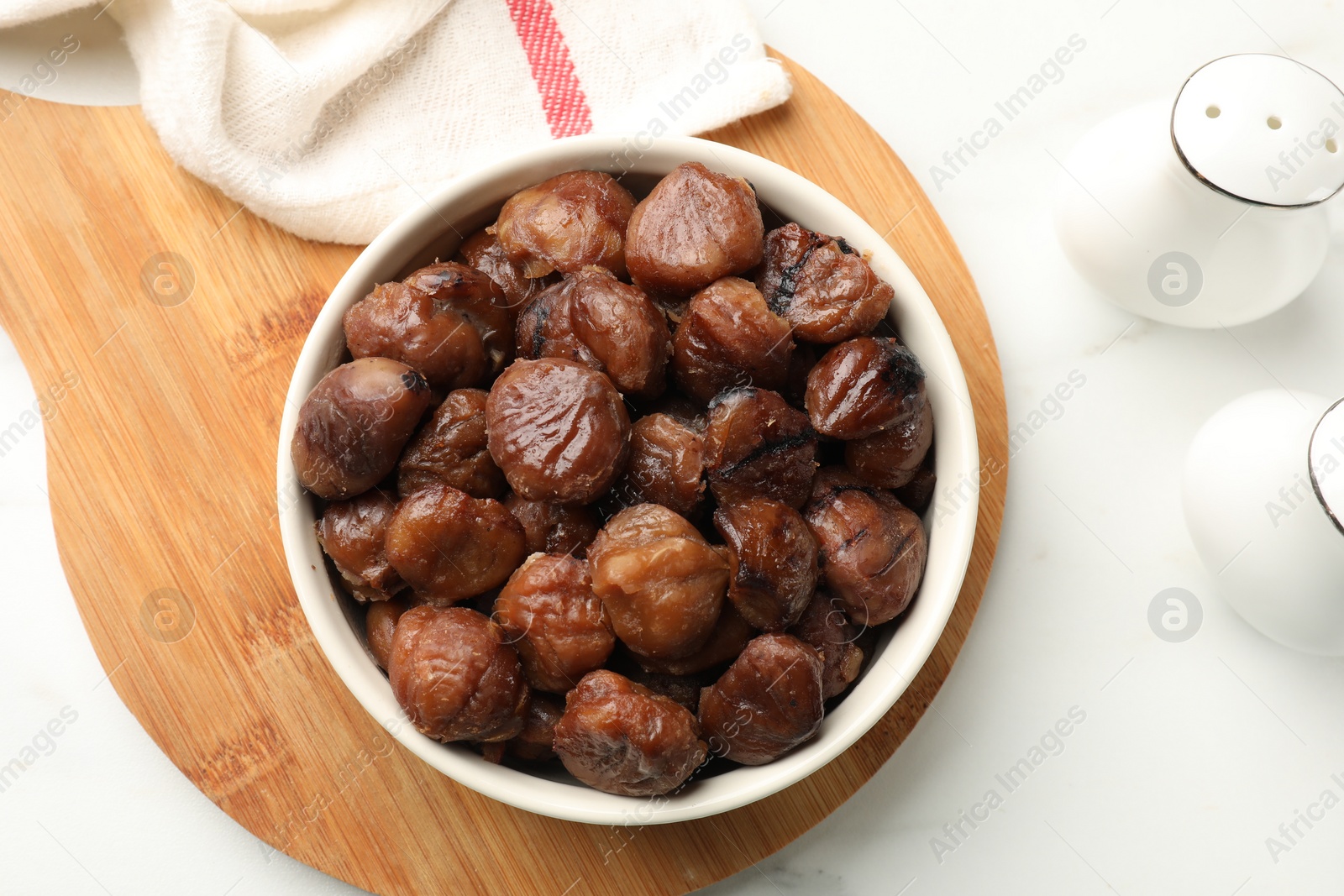 Photo of Roasted edible sweet chestnuts in bowl on white marble table, top view