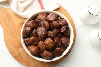 Photo of Roasted edible sweet chestnuts in bowl on white marble table, top view