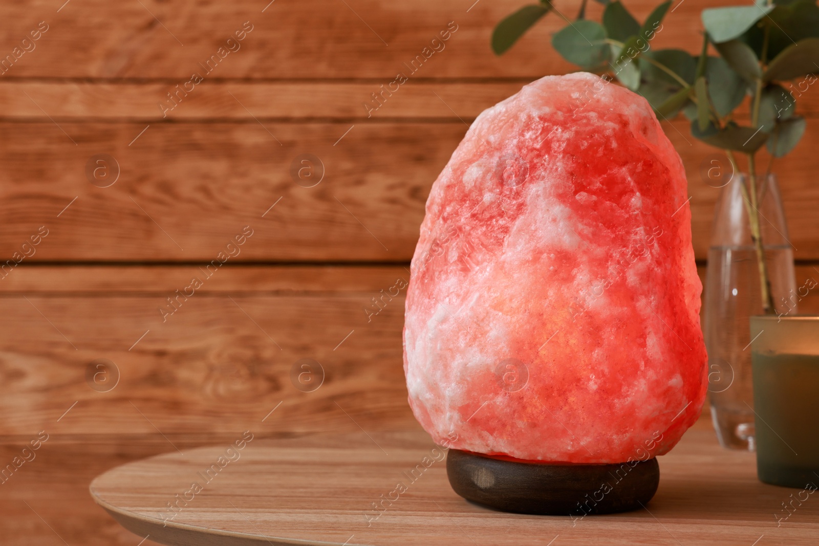 Photo of Beautiful Himalayan salt lamp, eucalyptus branches and candle on wooden table indoors, space for text