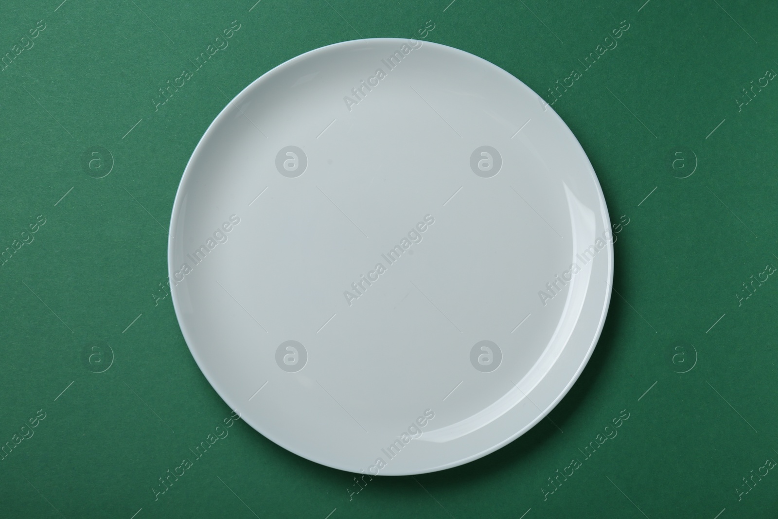 Photo of Empty white ceramic plate on green background, top view