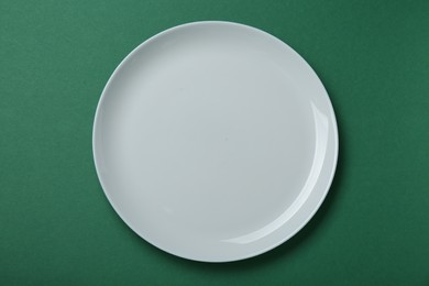 Photo of Empty white ceramic plate on green background, top view