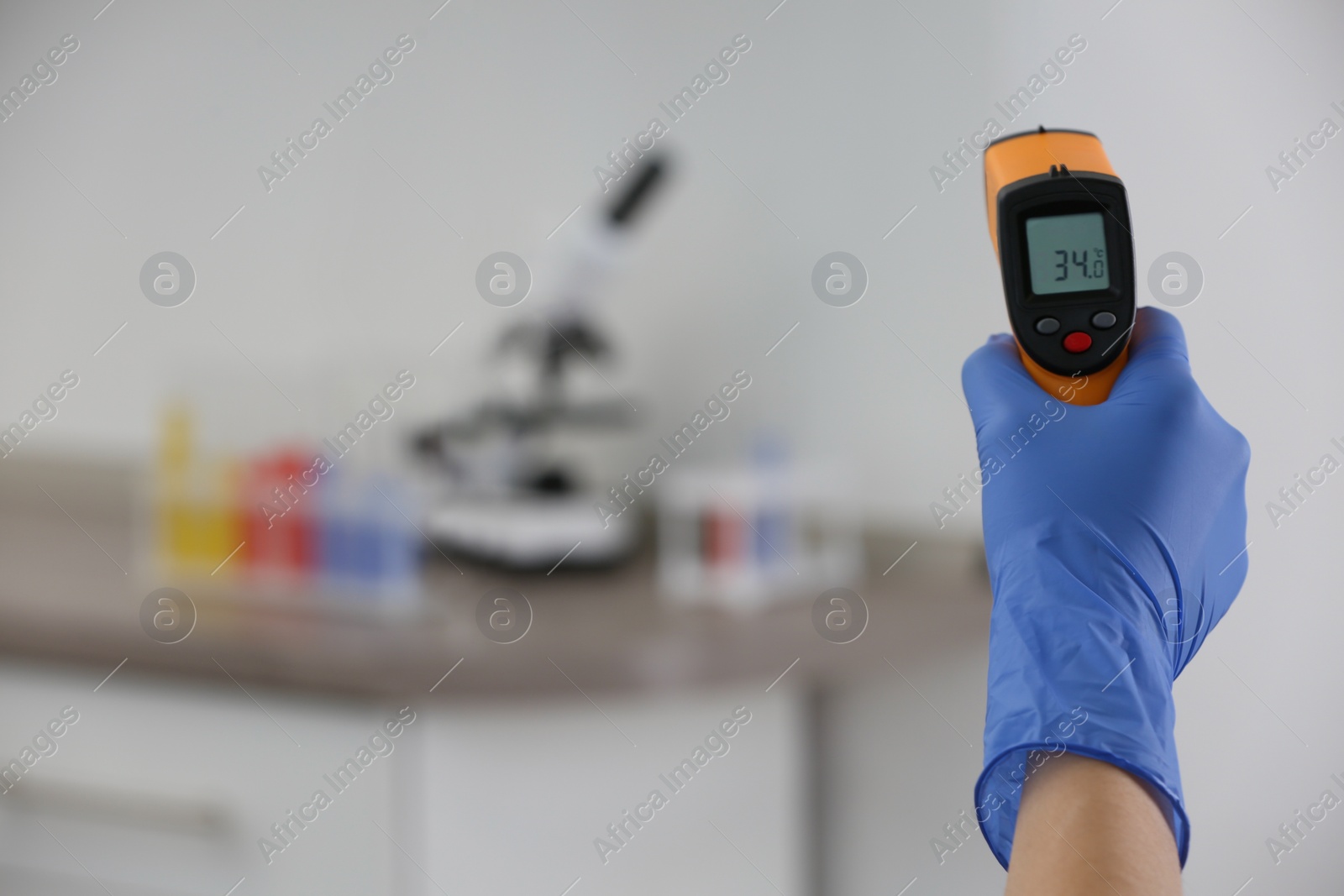 Photo of Closeup view of doctor with infrared thermometer on blurred background, space for text. Checking temperature during Covid-19 pandemic