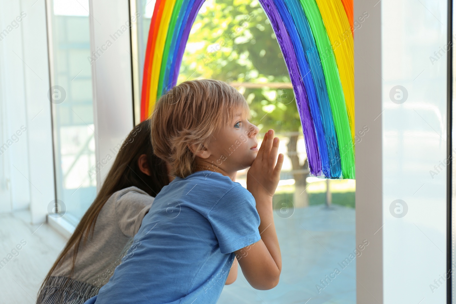 Photo of Little children near rainbow painting on window indoors. Stay at home concept