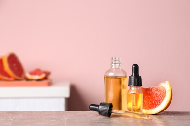 Bottles of essential oil and grapefruit slices on table against blurred background. Space for text