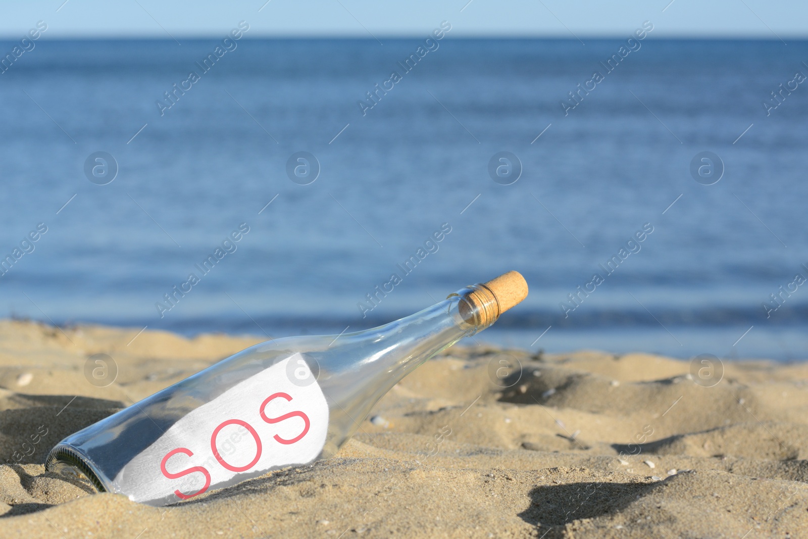 Photo of Glass bottle with SOS message on sand near sea, space for text