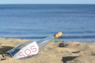 Glass bottle with SOS message on sand near sea, space for text