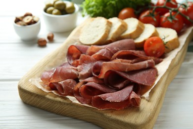 Board with delicious bresaola on white wooden table, closeup