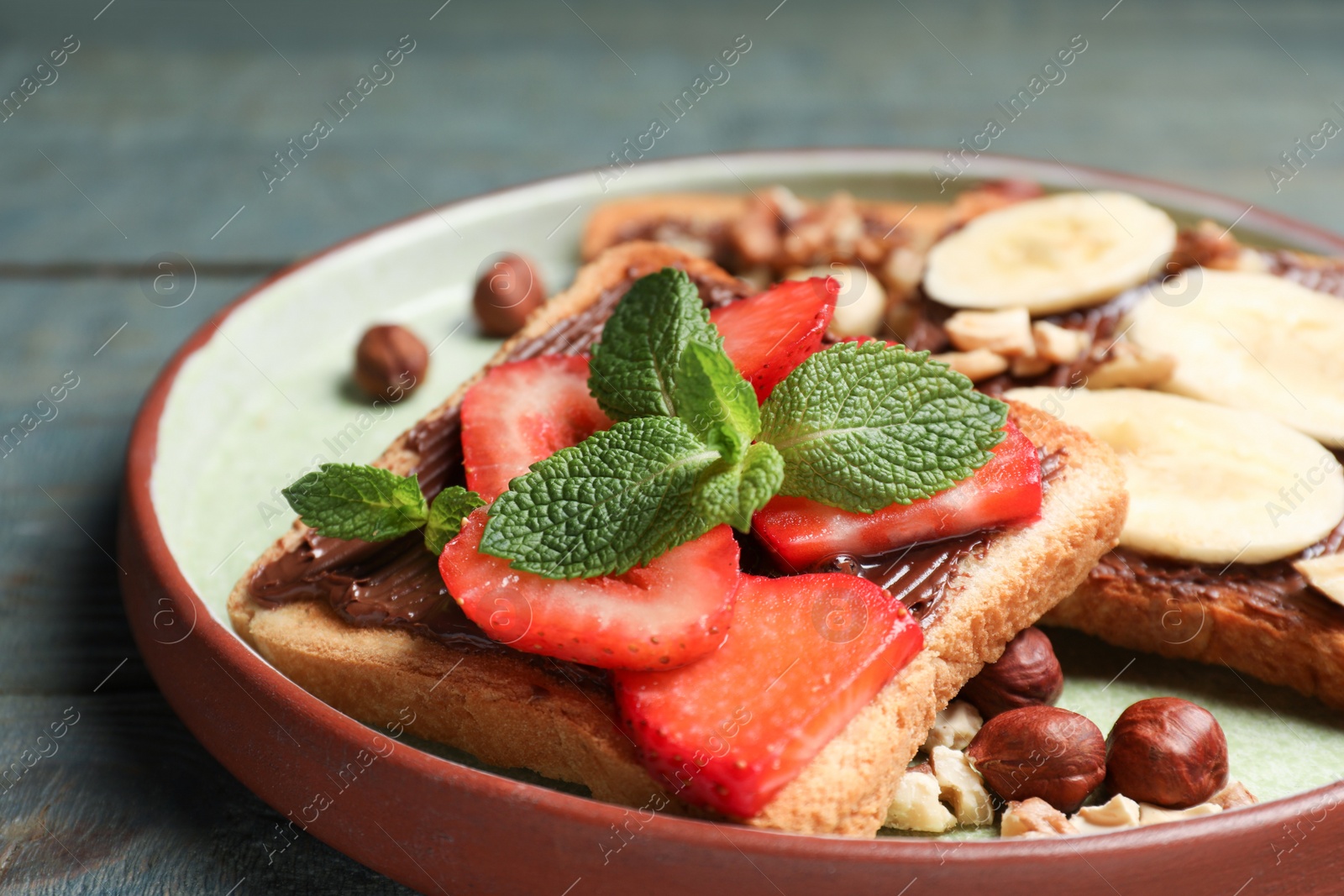 Photo of Tasty toasts with chocolate spread, nuts, strawberries, banana and mint served on wooden table, closeup