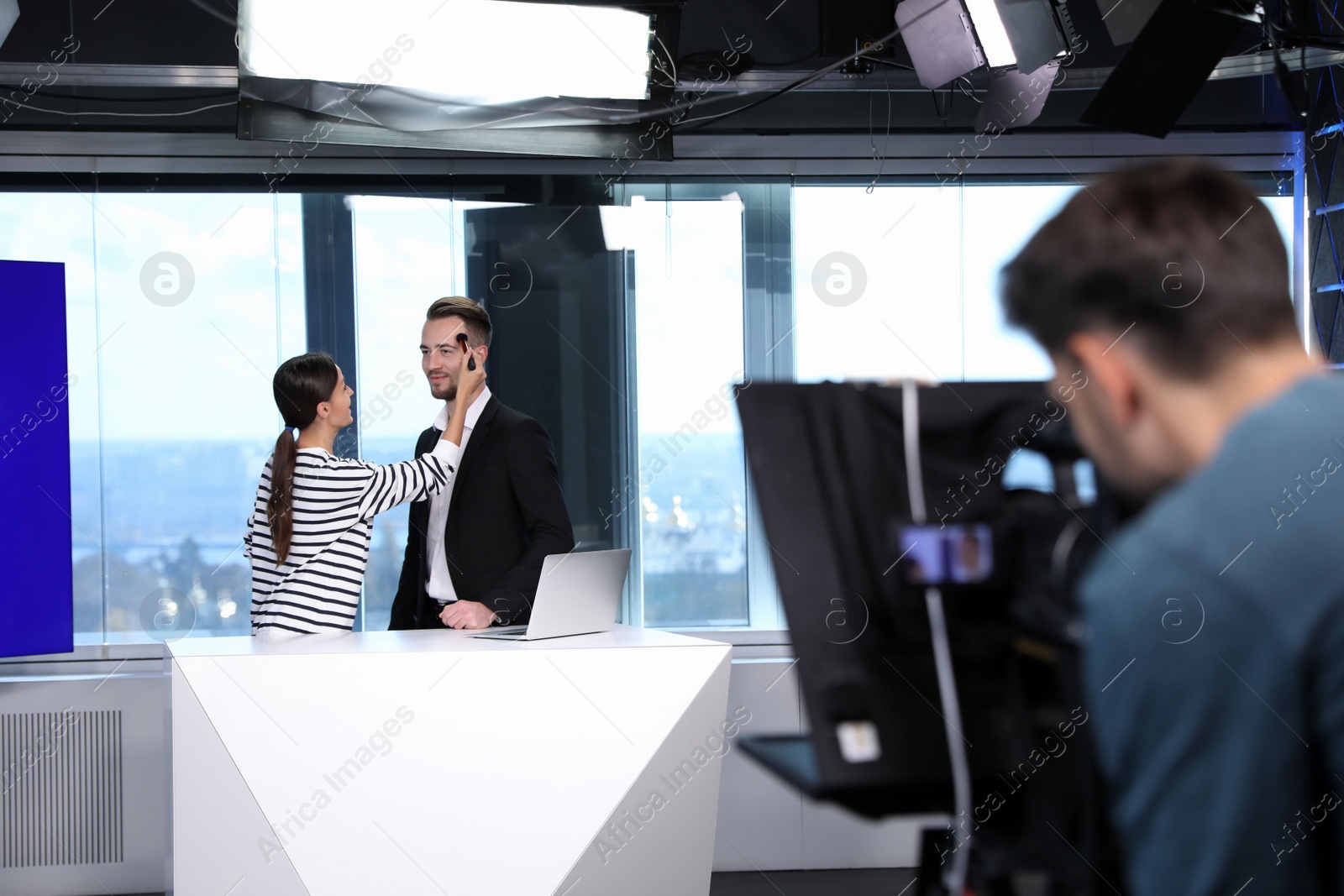 Photo of Presenter, makeup artist and video camera operator working in studio. News broadcasting