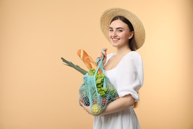 Photo of Woman with string bag of fresh vegetables and baguette on beige background, space for text