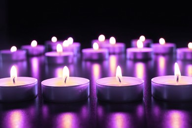 Image of Beautiful burning violet candles on black background. Funeral attributes