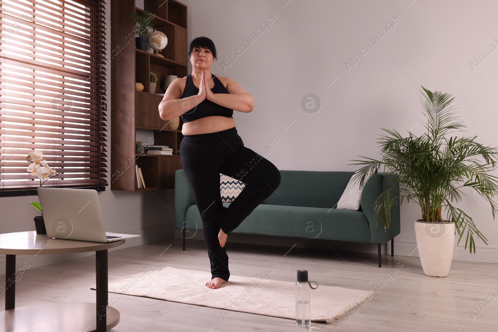 Photo of Overweight mature woman practicing yoga on rug at home