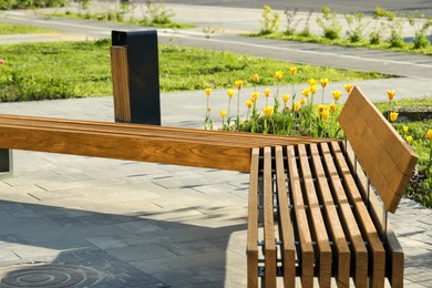 Wooden bench and trash bin in city park on sunny morning