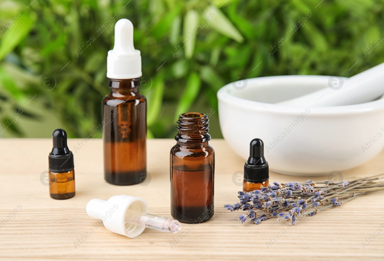 Photo of Bottles with natural herbal oil and lavender flowers on table against blurred background