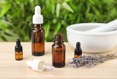 Bottles with natural herbal oil and lavender flowers on table against blurred background