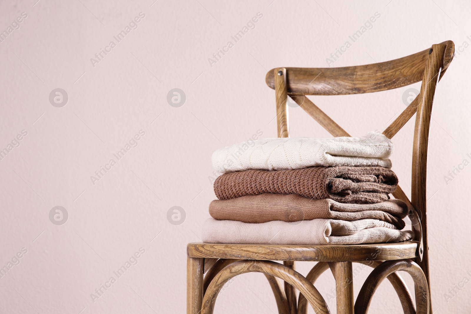 Photo of Stack of folded warm sweaters on wooden chair against light background. Space for text