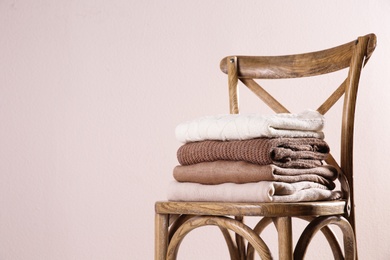 Stack of folded warm sweaters on wooden chair against light background. Space for text