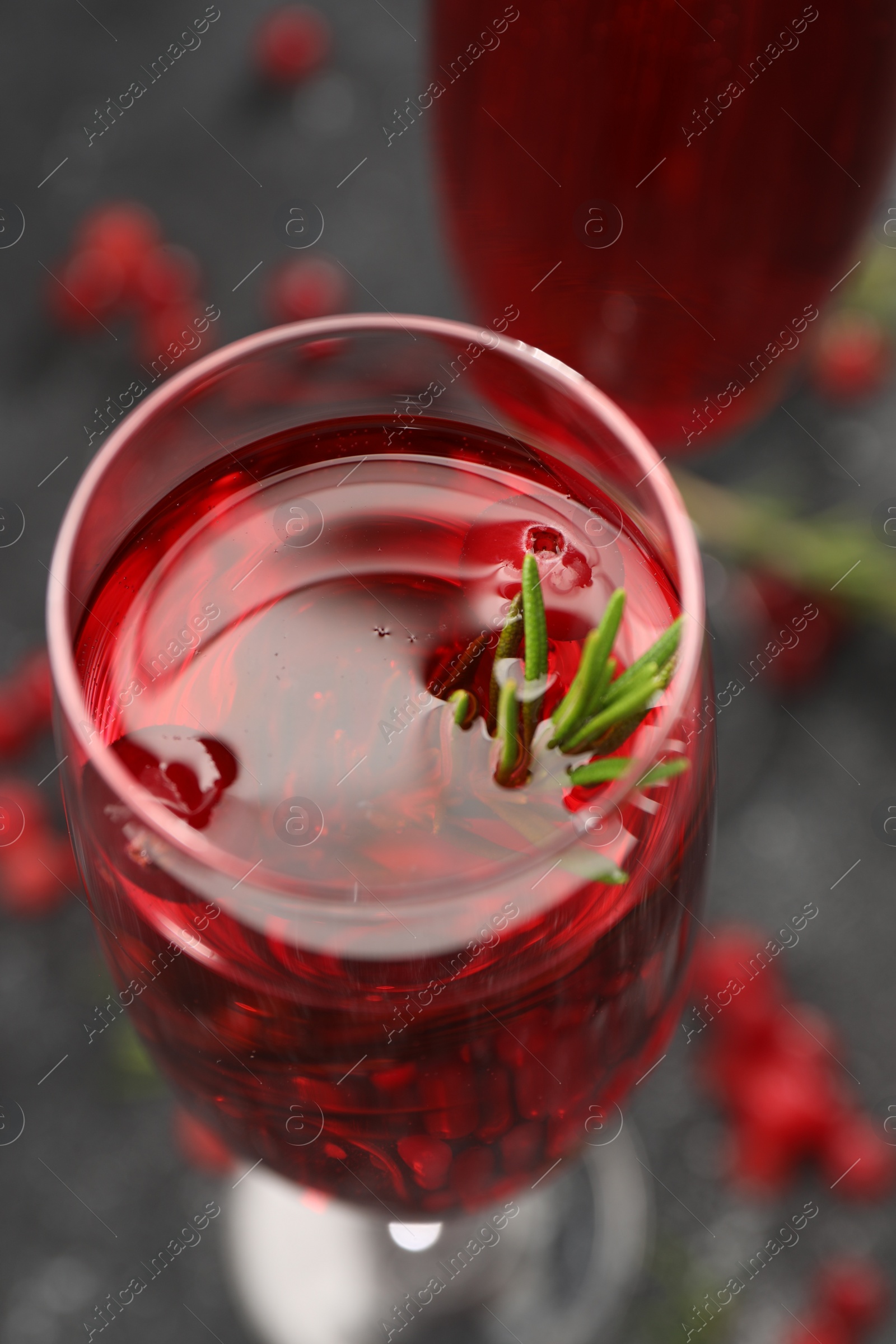 Photo of Tasty cranberry cocktail with rosemary in glass on gray table, closeup