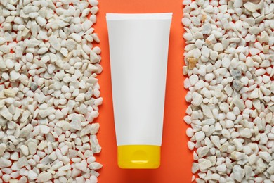 Photo of Tube of suntan cream and white marble pebbles on orange background, flat lay