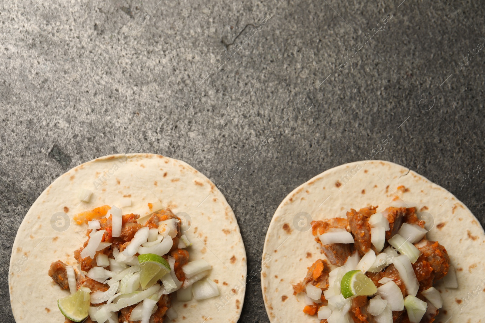 Photo of Delicious tacos with vegetables, meat and lime on grey textured table, flat lay. Space for text