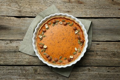 Delicious pumpkin pie with seeds and hazelnuts on wooden table, top view