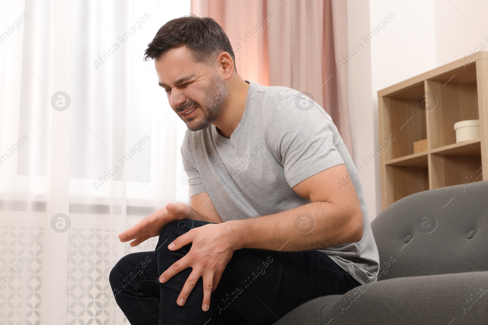 Photo of Man suffering from knee pain on sofa indoors