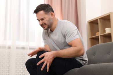 Man suffering from knee pain on sofa indoors