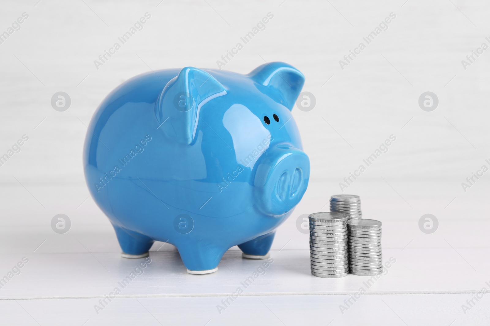 Photo of Financial savings. Piggy bank and stacked coins on white wooden table