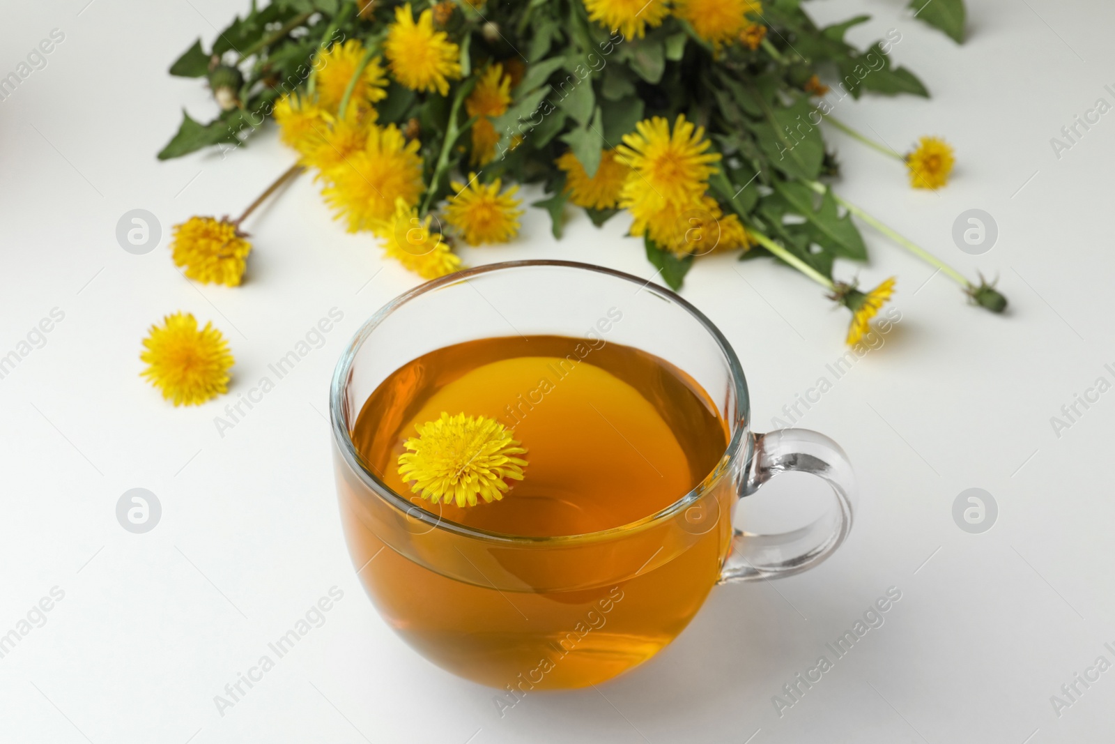 Photo of Delicious fresh tea and beautiful dandelion flowers on white background