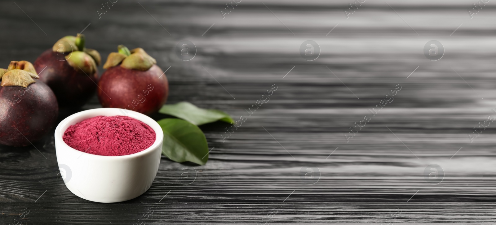 Photo of Purple mangosteen powder and fruits on black wooden table. Space for text