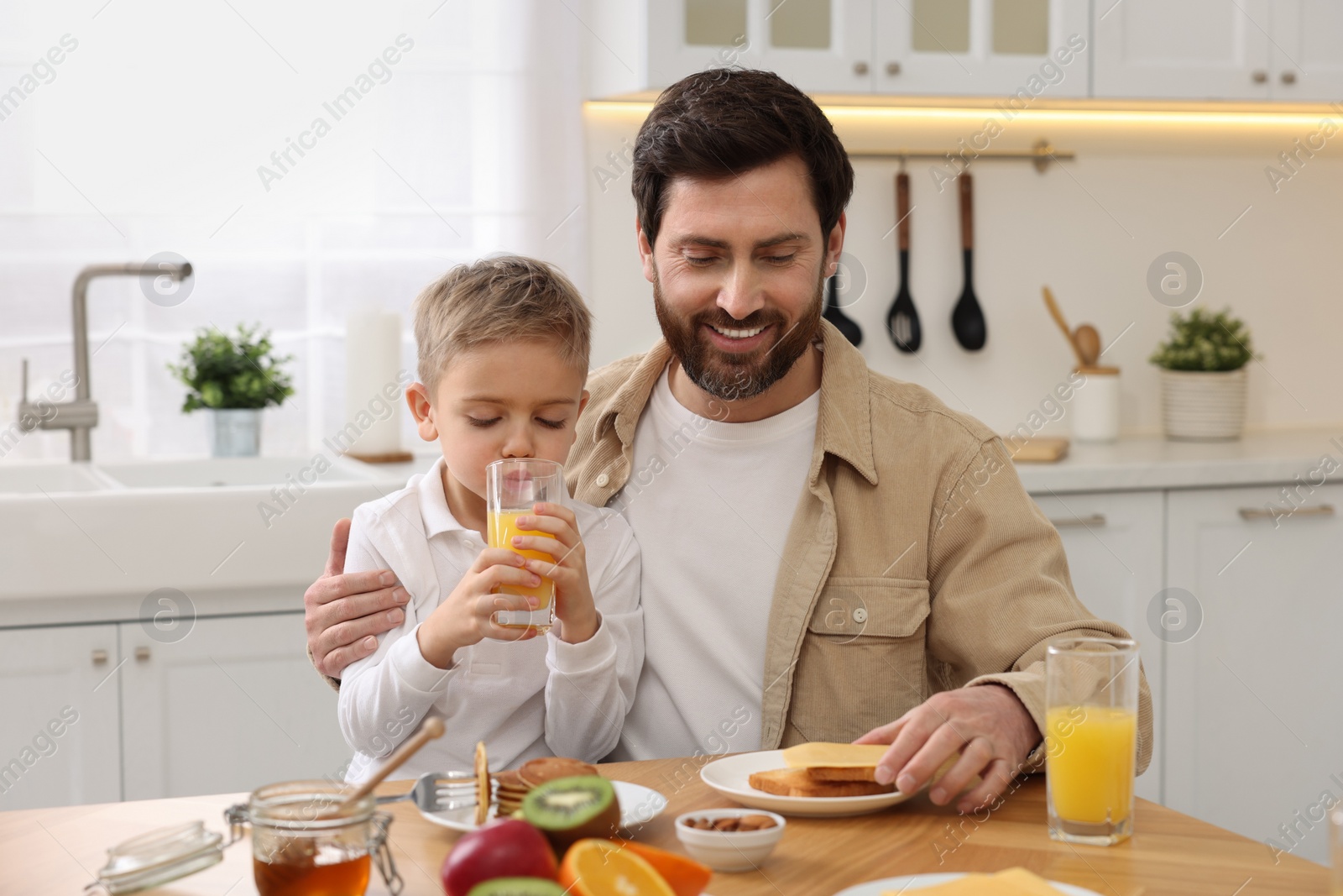 Photo of Father and his cute little son having breakfast at table in kitchen