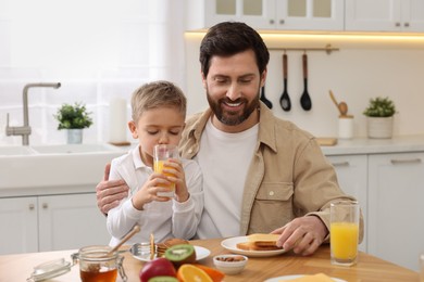 Photo of Father and his cute little son having breakfast at table in kitchen