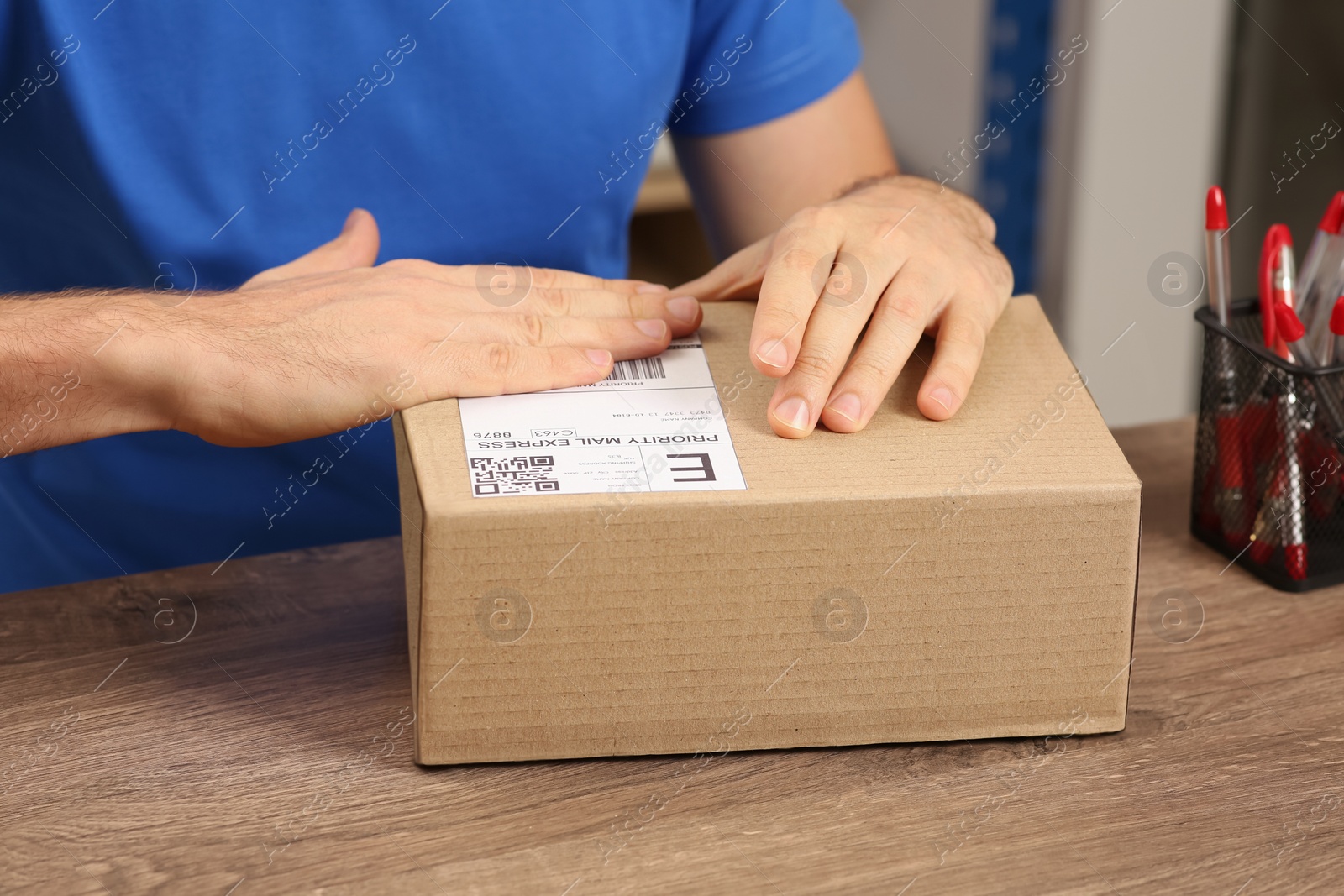 Photo of Post office worker sticking barcode on parcel at counter indoors, closeup