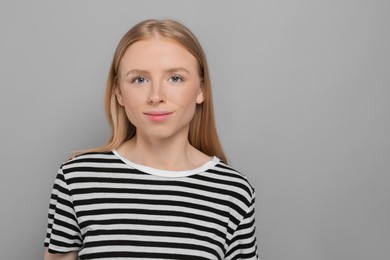 Portrait of beautiful young woman in striped t-shirt on grey background. Space for text