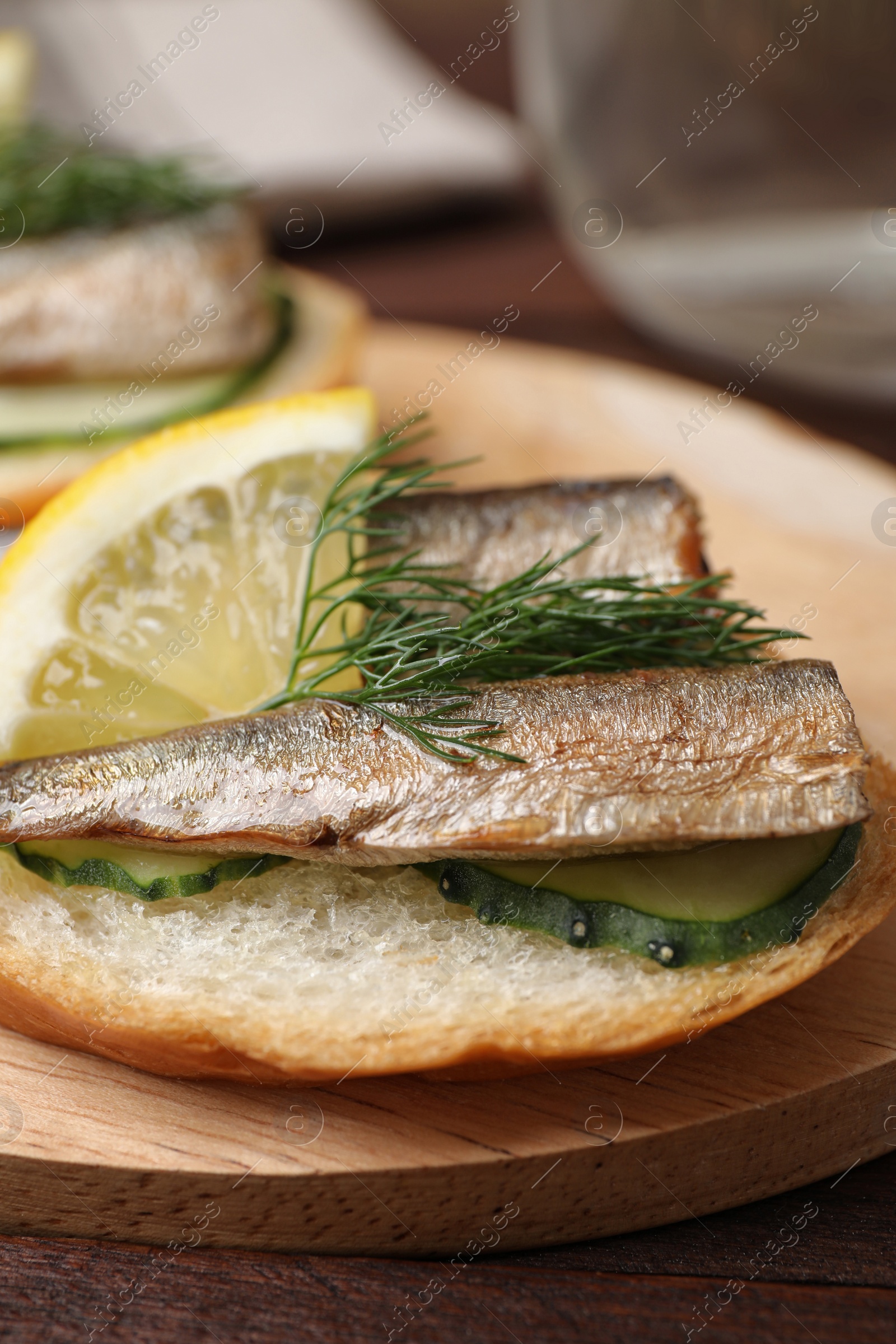 Photo of Delicious sandwich with sprats, cucumbers, lemon and dill on wooden board, closeup