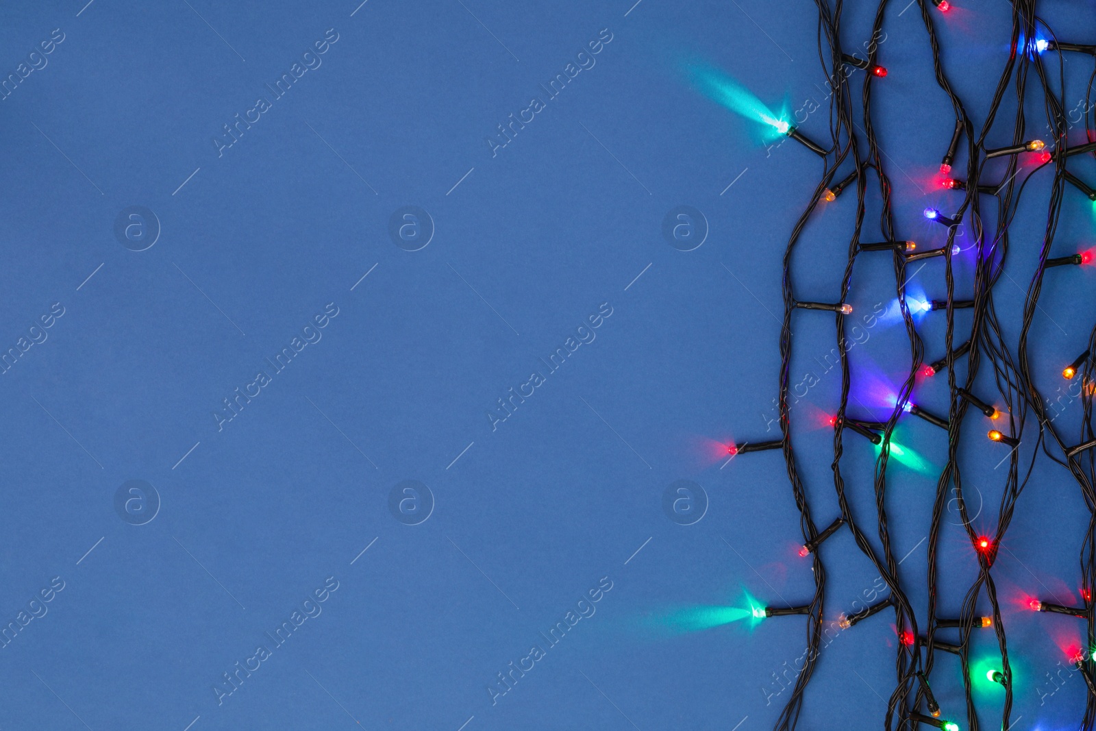 Photo of Christmas lights on blue background, top view. Space for text