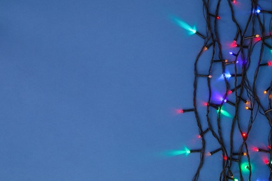 Photo of Christmas lights on blue background, top view. Space for text